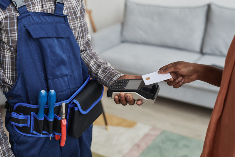 Close up of unrecognizable woman paying handyman for services by swiping card over bank terminal, copy space