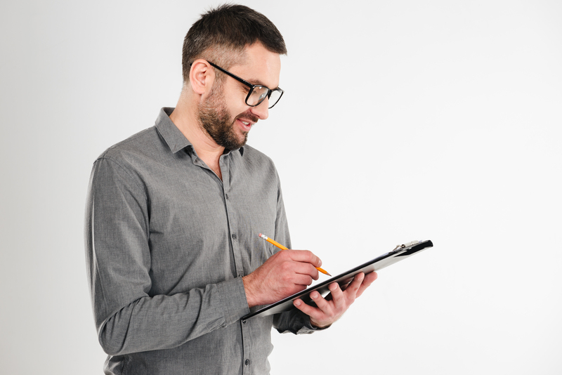 Image of handsome businessman standing isolated over white background. Looking aside holding clipboard writing notes.