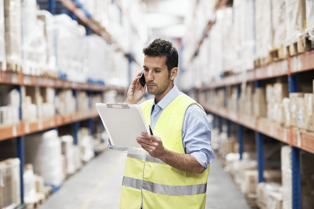 A young man in a warehouse taking orders on his mobile phone