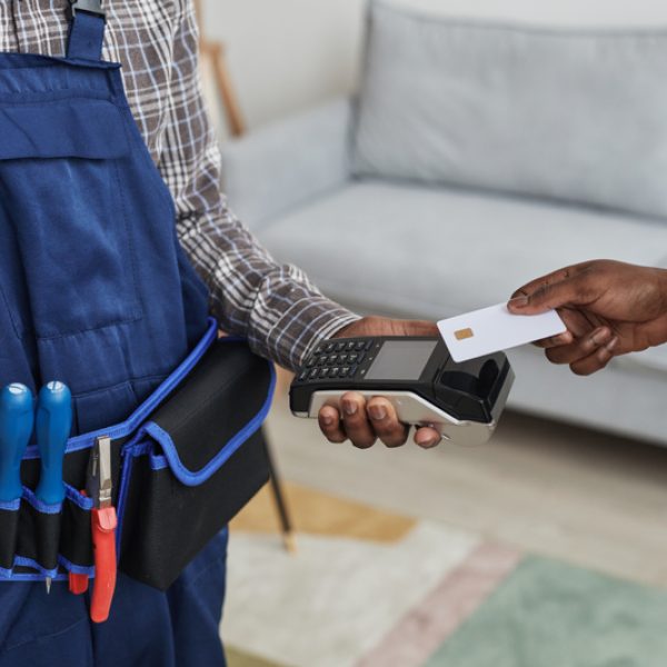 Close up of unrecognizable woman paying handyman for services by swiping card over bank terminal, copy space